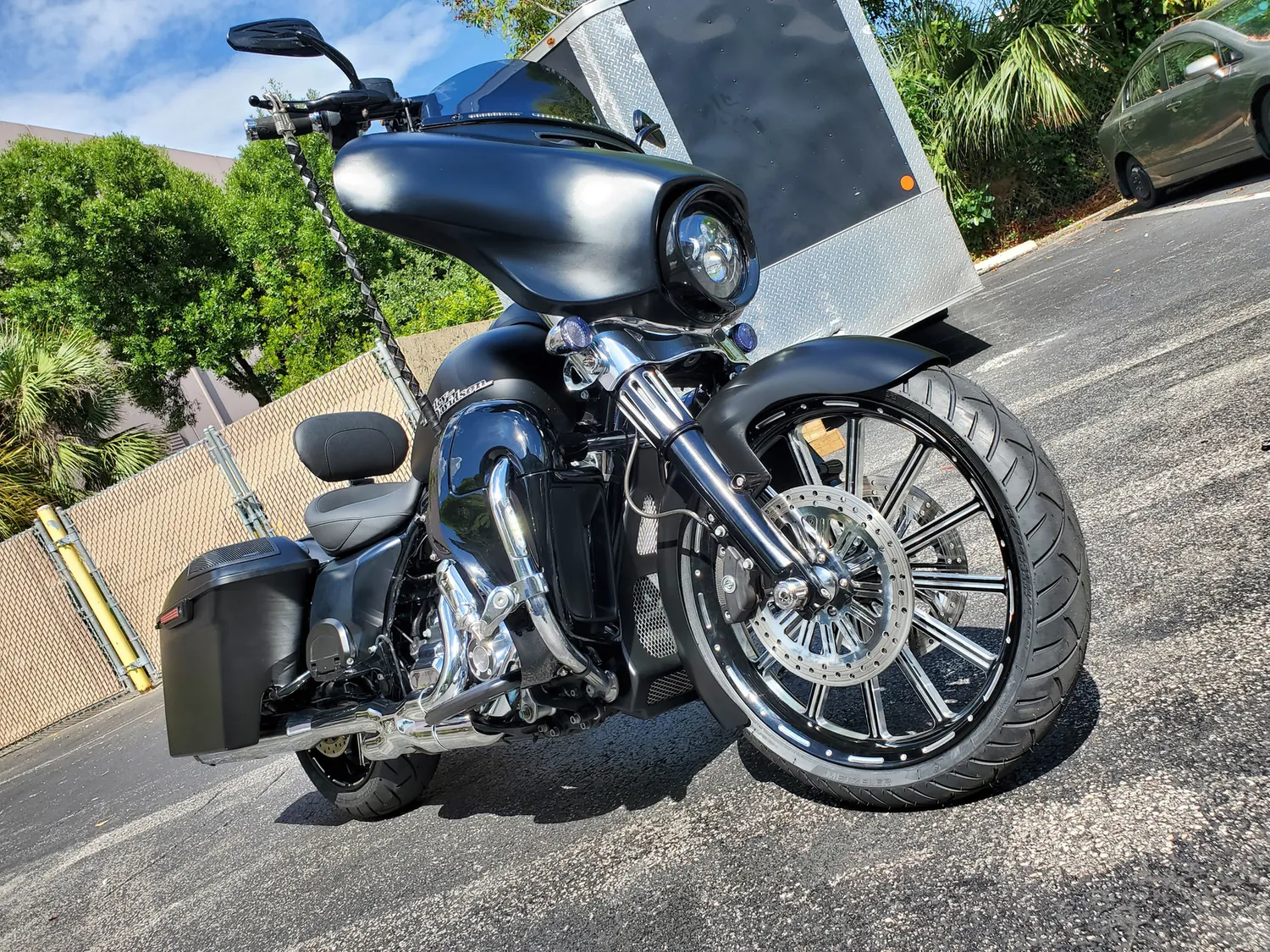 Matte black custom Harley bagger with a big black front wheel and ape hangers